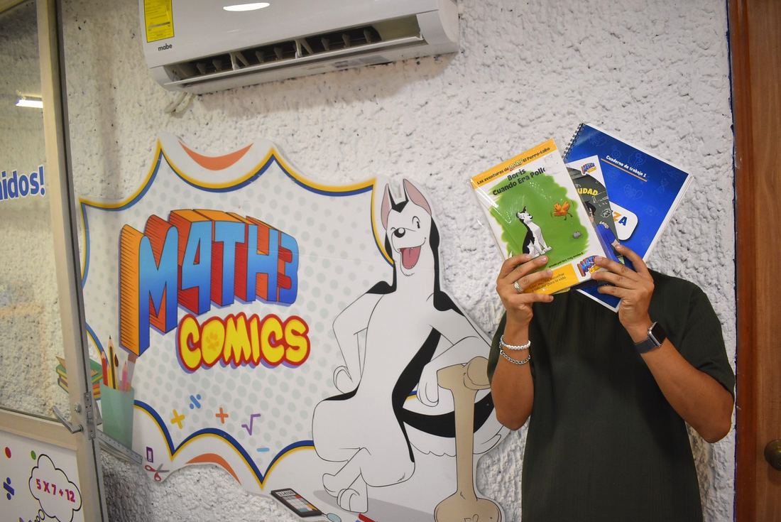 Alumno sosteniendo material de MatheComics frente al mural de la marca en sucursal.